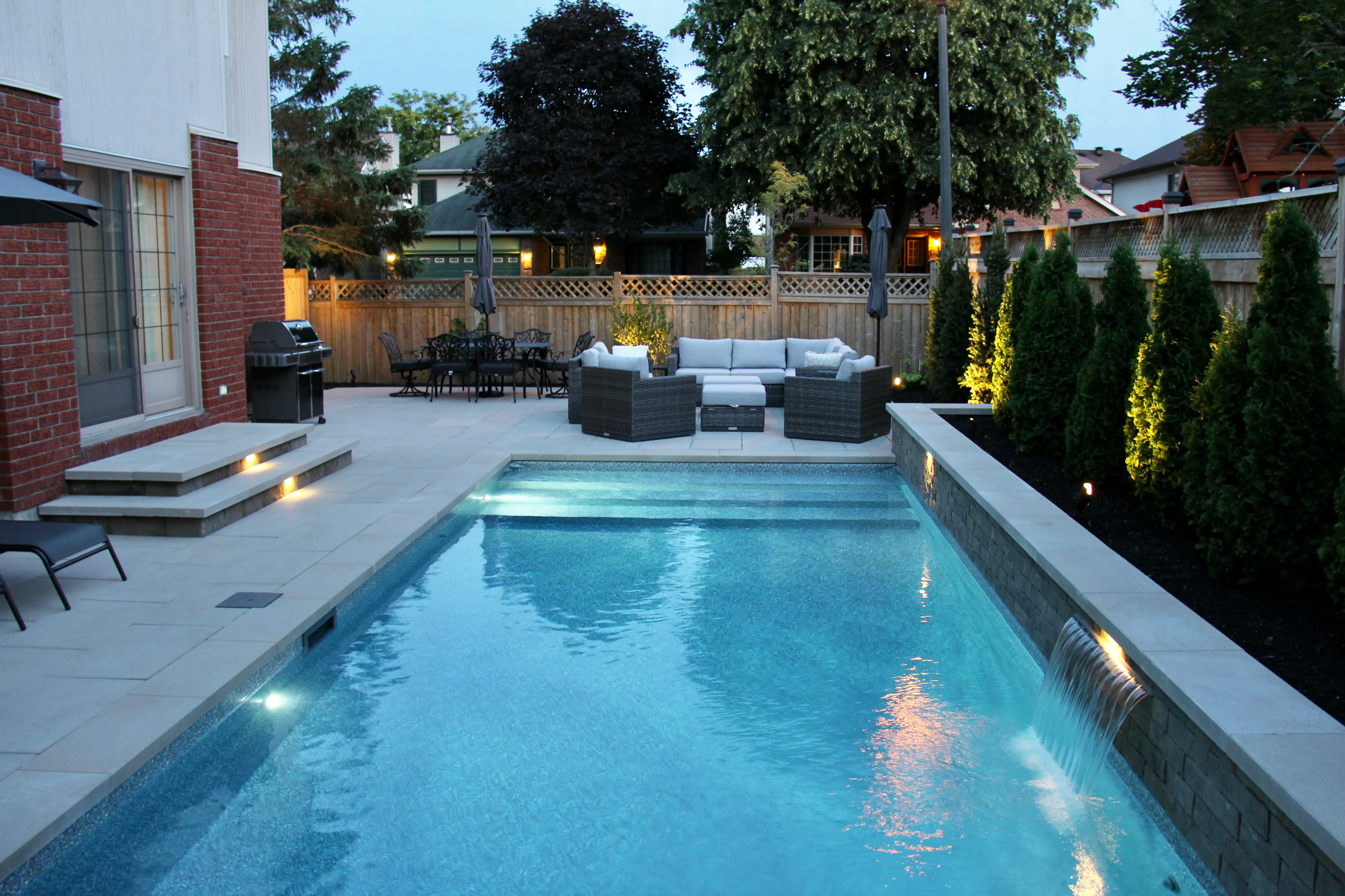 Illuminated inground pool and backyard at blue hour