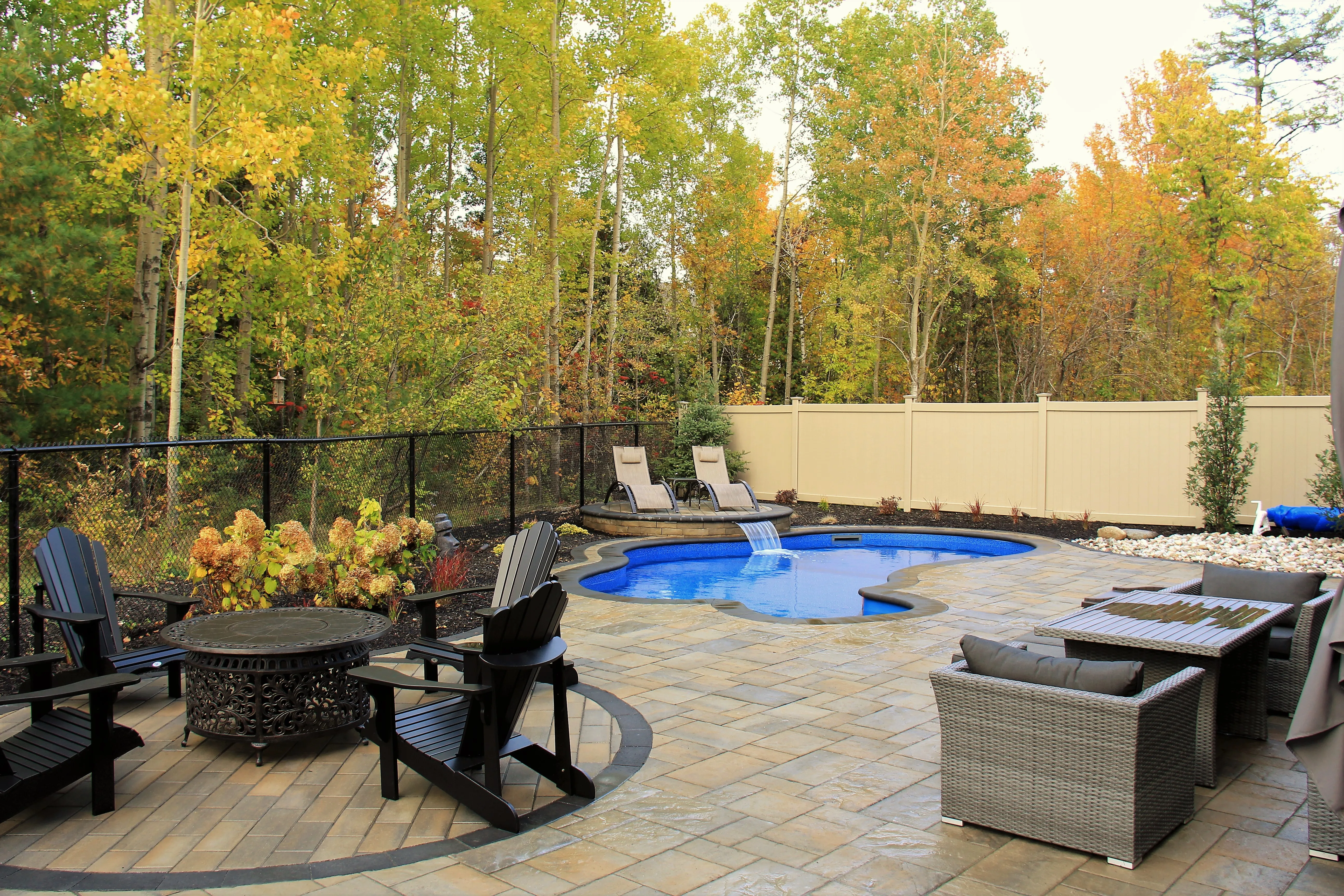 Curved inground pool and waterfall surrounded by autumn trees